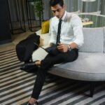 A young businessman in formal attire reading a magazine on a modern sofa in a stylish interior.