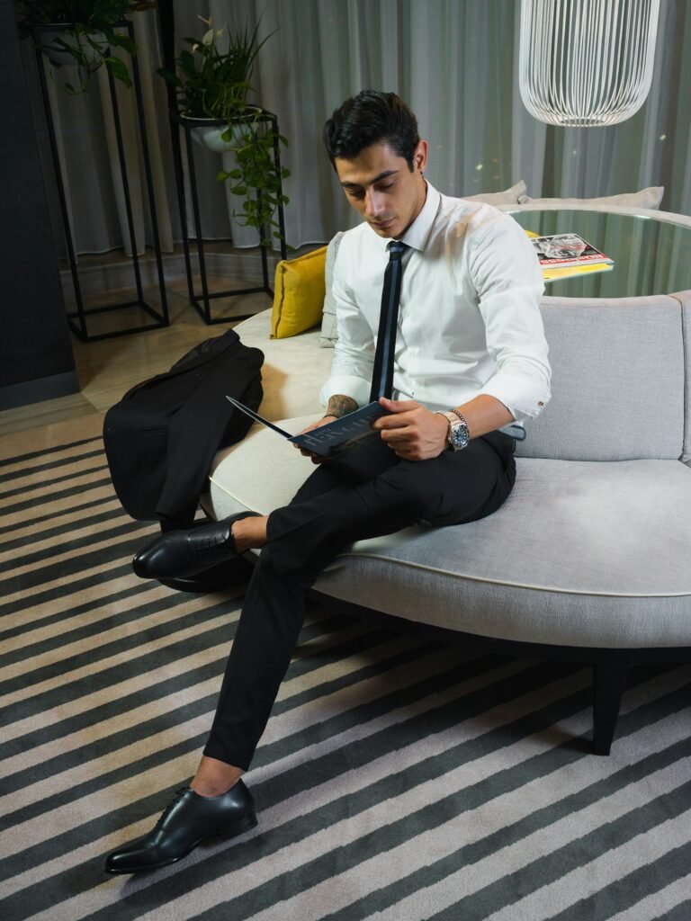 A young businessman in formal attire reading a magazine on a modern sofa in a stylish interior.