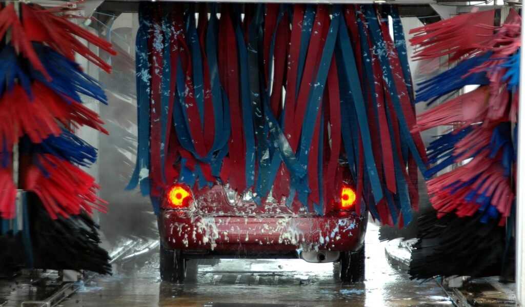 Red car being cleaned in an automated car wash with colorful brushes and soap suds.