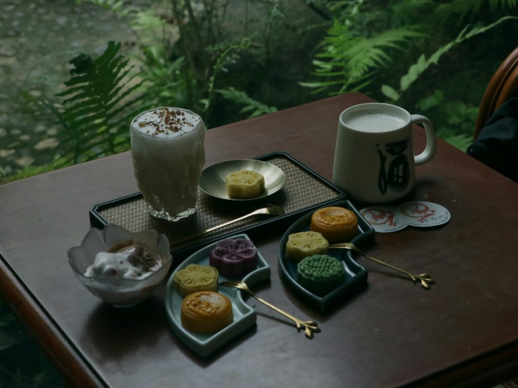 Elegant display of mooncakes and beverages on a wooden table with a green nature backdrop.