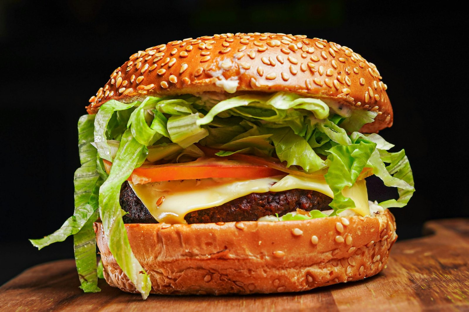 Appetizing close-up of a cheeseburger with lettuce, tomato, and sesame seed bun.