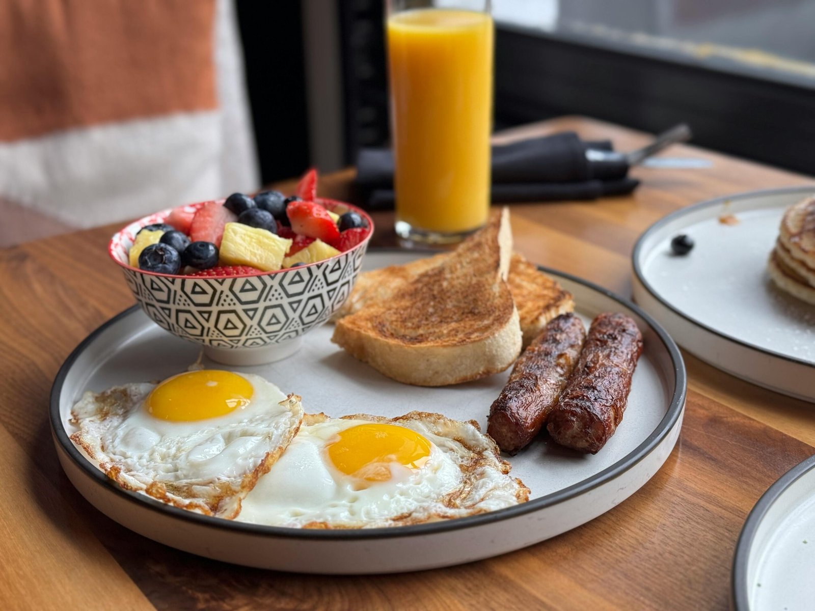 A hearty breakfast with sunny side eggs, fruit bowl, toast, and orange juice.